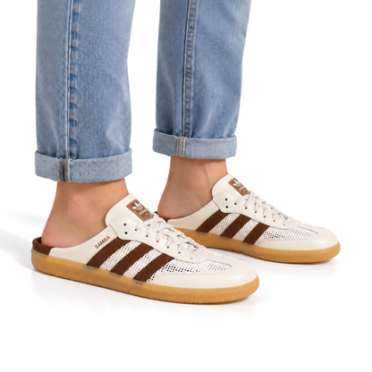 Adult wearing off-white and brown adidas Samba Mules with cuffed light blue jeans and bare ankles.