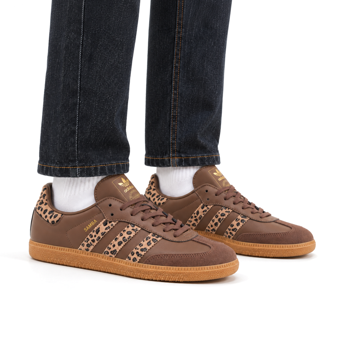 Brown leopard-print adidas Samba OG sneakers worn with dark denim trousers and white socks, with both toes facing right.